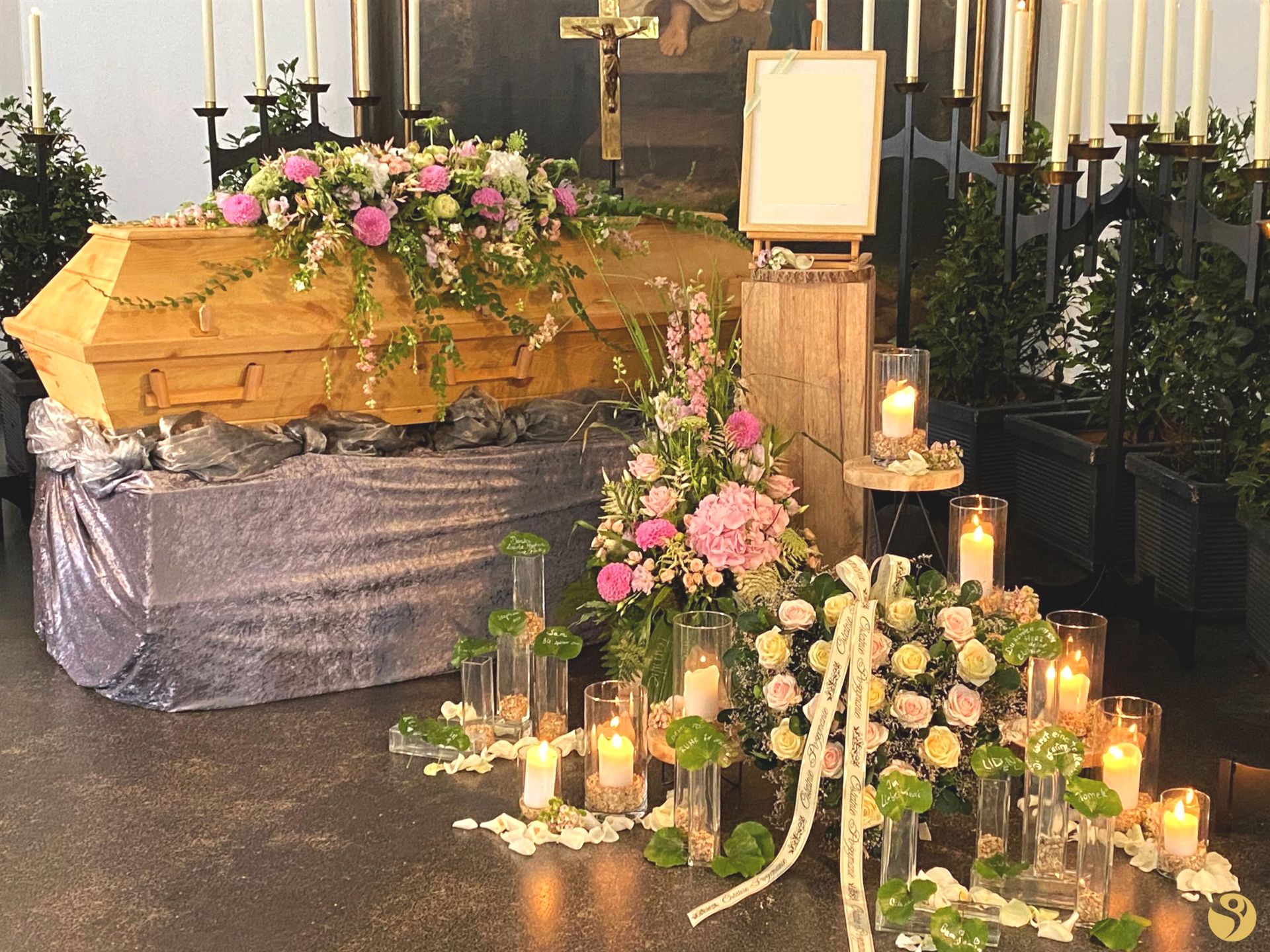 Sarg mit zartem floralem Sargschmuck in Rosa und Creme, umgeben von Kerzen