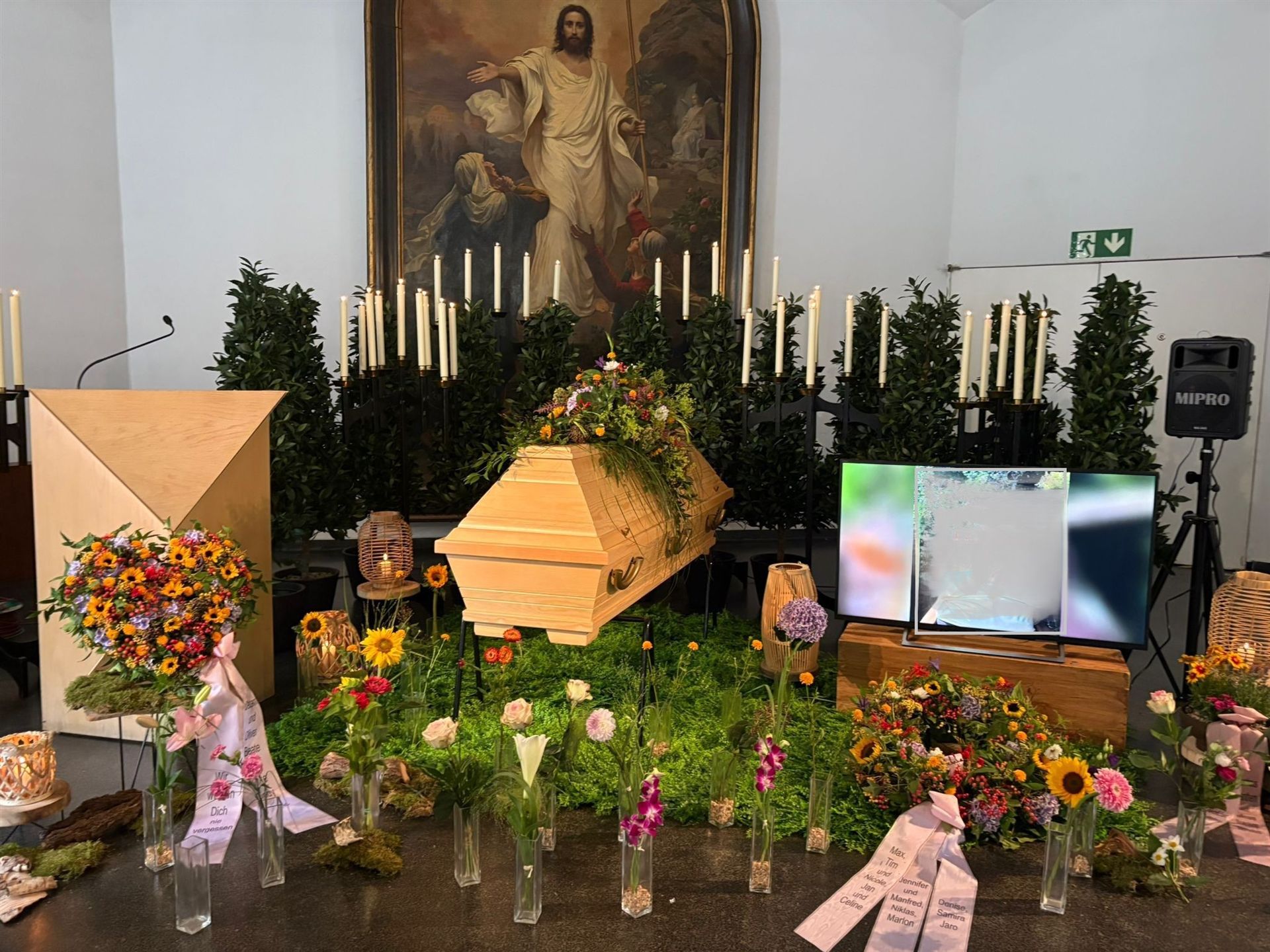 Naturnahe florale Dekoration rund um den Sarg mit Kerzen und Blumen in Vasen